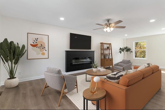 living room featuring a glass covered fireplace, recessed lighting, wood finished floors, and baseboards