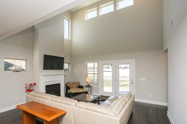 living room featuring a glass covered fireplace, dark wood-type flooring, baseboards, and a towering ceiling