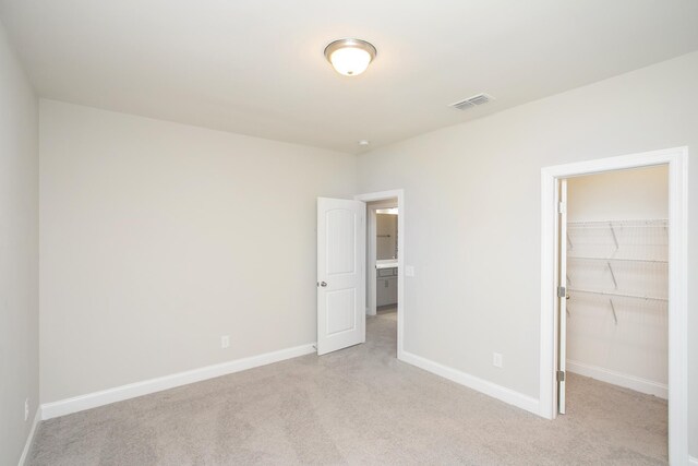 unfurnished bedroom with visible vents, baseboards, a closet, a walk in closet, and light colored carpet