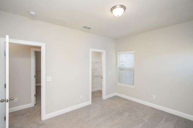 unfurnished bedroom with a spacious closet, visible vents, light colored carpet, and baseboards