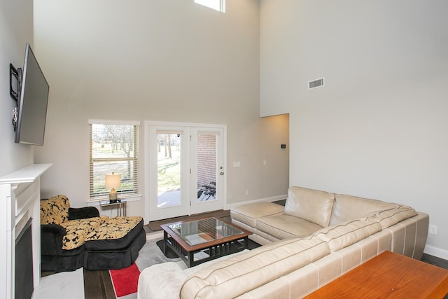 living area with visible vents, baseboards, a fireplace, a towering ceiling, and wood finished floors