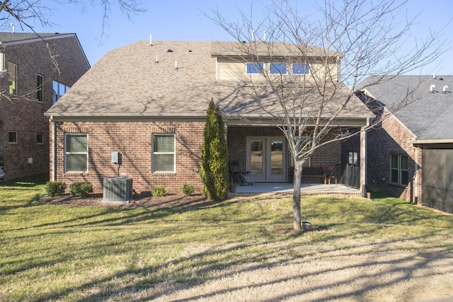 rear view of property featuring a shingled roof, french doors, brick siding, and a lawn