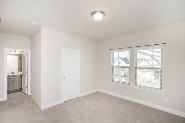 spare room with light colored carpet, baseboards, and a sink