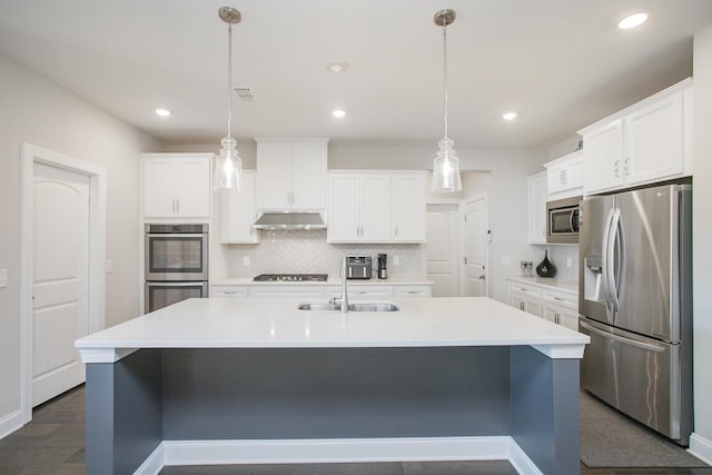 kitchen with a center island with sink, under cabinet range hood, a sink, backsplash, and stainless steel appliances