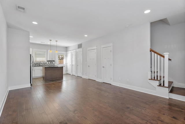 unfurnished living room featuring visible vents, a sink, dark wood finished floors, stairway, and baseboards