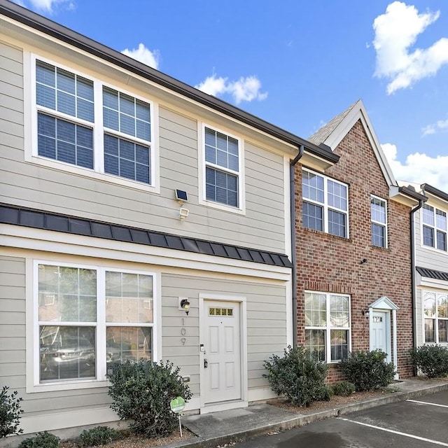 multi unit property with a standing seam roof, uncovered parking, brick siding, and metal roof