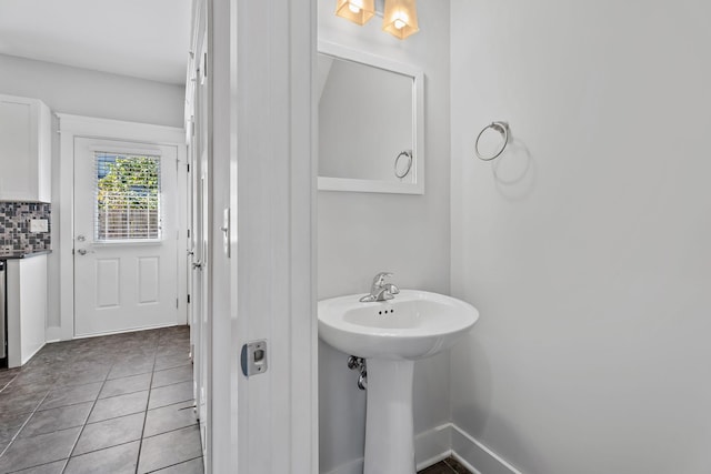 bathroom with decorative backsplash, tile patterned floors, baseboards, and a sink