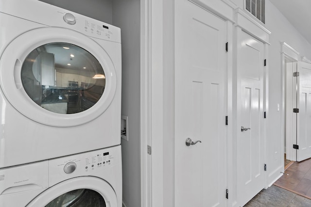 clothes washing area featuring visible vents, stacked washing maching and dryer, and laundry area