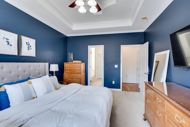 bedroom with a ceiling fan, baseboards, ornamental molding, a raised ceiling, and connected bathroom