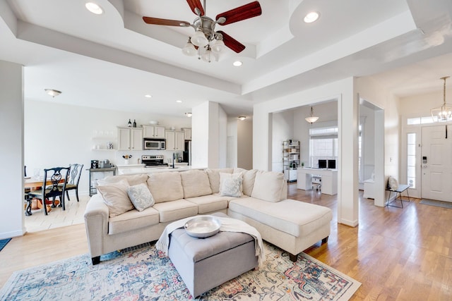 living room with a ceiling fan, baseboards, a tray ceiling, recessed lighting, and light wood-style floors