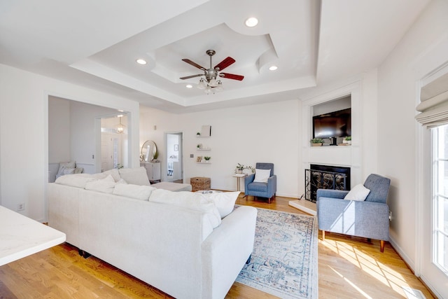 living room featuring recessed lighting, a raised ceiling, light wood-style floors, and a fireplace with raised hearth