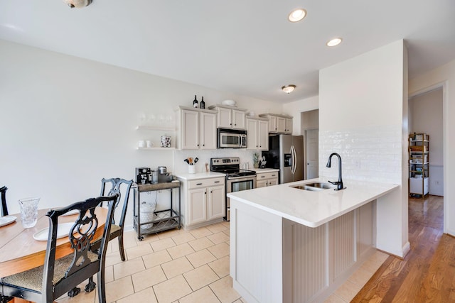 kitchen with a sink, decorative backsplash, appliances with stainless steel finishes, and a peninsula