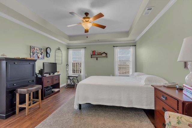 bedroom featuring visible vents, a tray ceiling, wood finished floors, crown molding, and baseboards