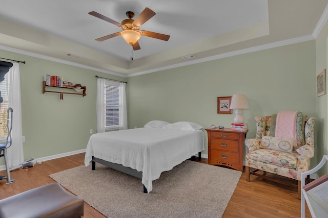 bedroom with baseboards, ornamental molding, wood finished floors, a raised ceiling, and a ceiling fan