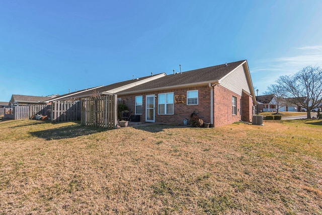 rear view of property with brick siding, central AC, a lawn, and fence