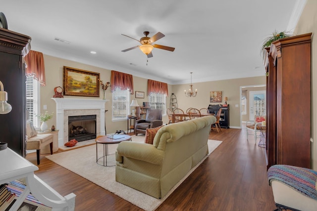 living area with dark wood-style floors, visible vents, baseboards, a high end fireplace, and ceiling fan with notable chandelier