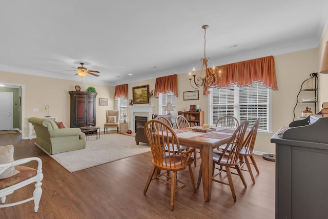 dining room featuring wood finished floors, baseboards, a fireplace, ornamental molding, and ceiling fan with notable chandelier