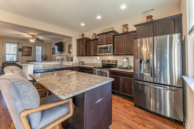 kitchen with dark brown cabinetry, open floor plan, appliances with stainless steel finishes, a peninsula, and a sink