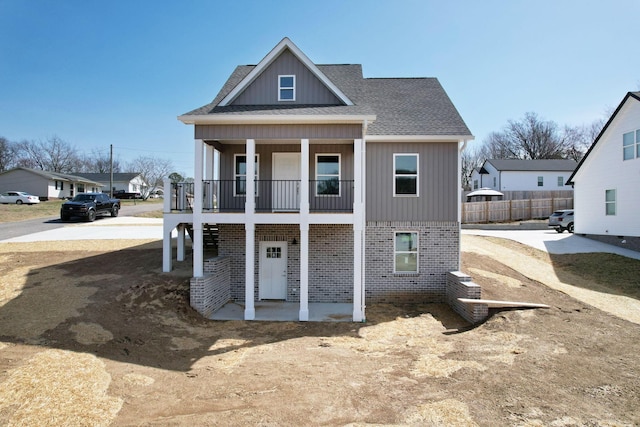 view of front of property with brick siding, board and batten siding, fence, roof with shingles, and a balcony