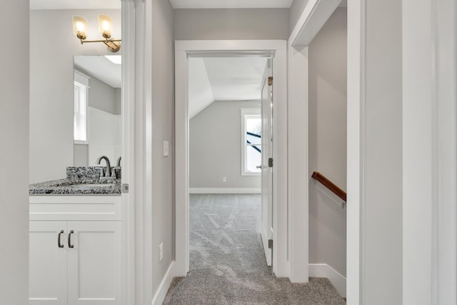 corridor with baseboards, light colored carpet, vaulted ceiling, an upstairs landing, and a sink