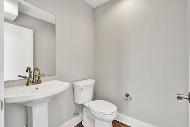 half bath featuring wood finished floors, toilet, baseboards, and a sink