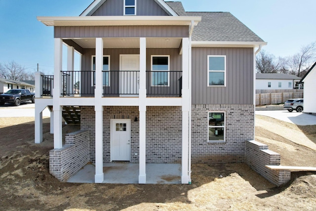 view of front facade with board and batten siding, a patio, brick siding, and roof with shingles