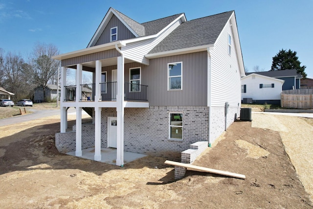 view of front of house featuring a balcony, a shingled roof, brick siding, central AC unit, and a patio area