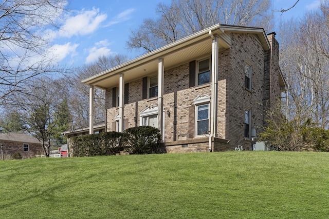 view of front facade with brick siding, a chimney, and a front yard