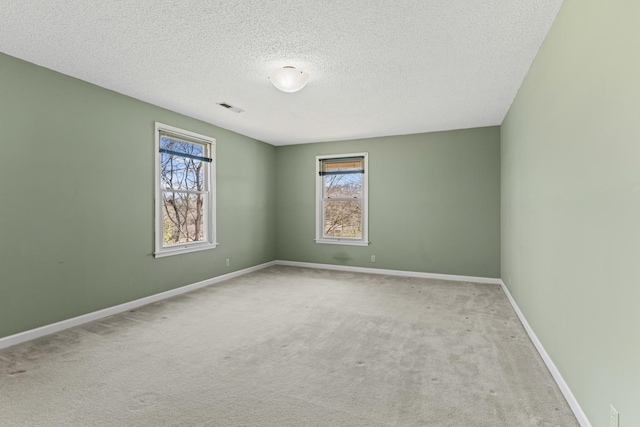 empty room with visible vents, a textured ceiling, baseboards, and carpet