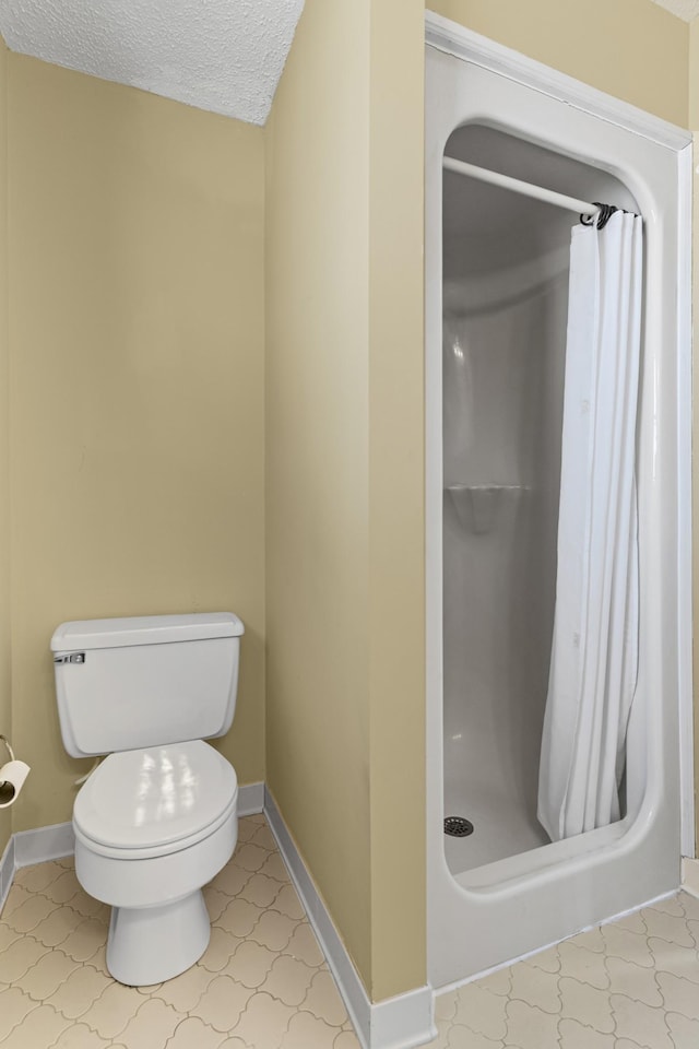 full bath featuring toilet, baseboards, a stall shower, and a textured ceiling