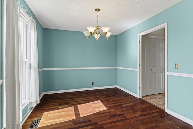 unfurnished room featuring wood finished floors, baseboards, visible vents, a textured ceiling, and a chandelier