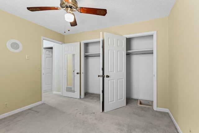 unfurnished bedroom featuring multiple closets, carpet, baseboards, and a textured ceiling