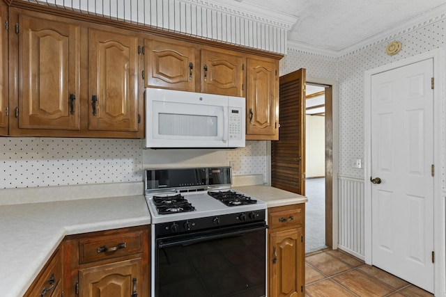 kitchen with range with gas stovetop, white microwave, wallpapered walls, ornamental molding, and light countertops