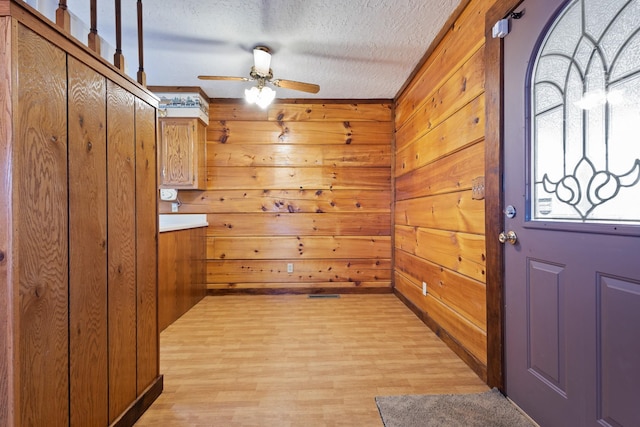 interior space featuring wooden walls, light wood-style flooring, a textured ceiling, and ceiling fan