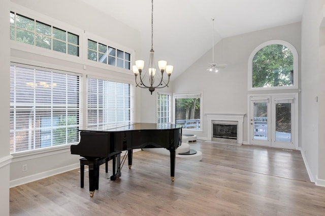 living area featuring baseboards, a fireplace with flush hearth, high vaulted ceiling, and light wood finished floors