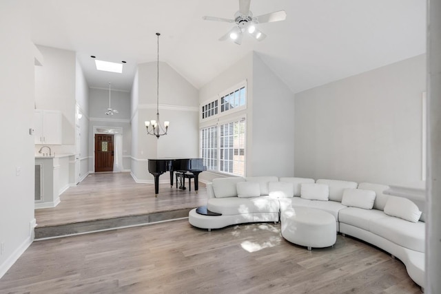 living area featuring visible vents, high vaulted ceiling, ceiling fan with notable chandelier, light wood-style floors, and a skylight