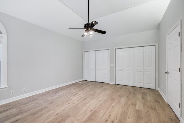 unfurnished bedroom featuring light wood-style flooring, baseboards, multiple closets, and ceiling fan