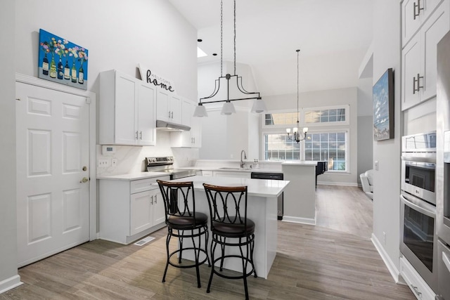 kitchen featuring under cabinet range hood, stainless steel electric stove, a center island, a peninsula, and light countertops