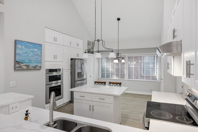 kitchen with light wood-type flooring, under cabinet range hood, light stone counters, white cabinetry, and appliances with stainless steel finishes