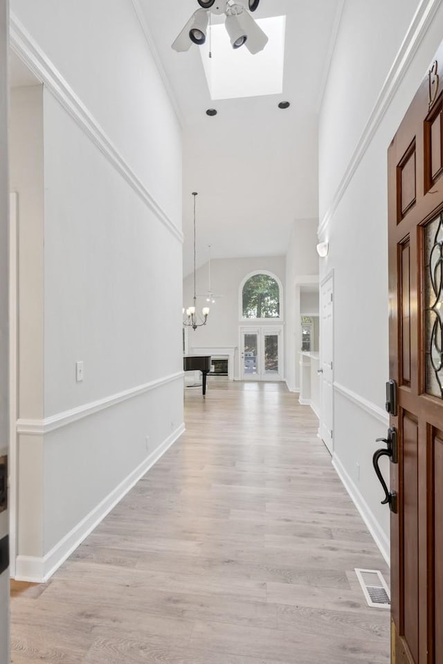 foyer with visible vents, light wood-style flooring, ceiling fan with notable chandelier, a high ceiling, and baseboards