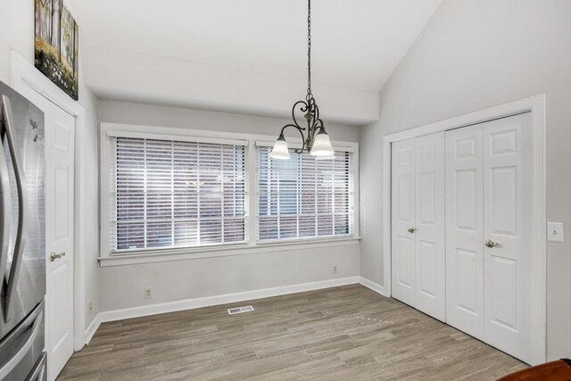 unfurnished dining area featuring lofted ceiling, light wood-style flooring, and baseboards