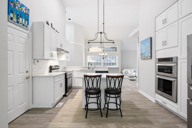 kitchen with light wood finished floors, a sink, stainless steel appliances, light countertops, and under cabinet range hood