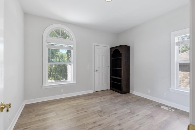 empty room featuring a wealth of natural light, visible vents, and light wood finished floors