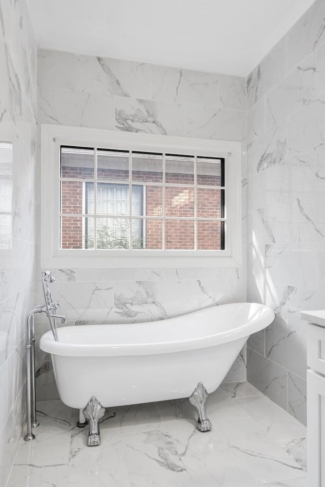 full bath with marble finish floor, stone wall, and a freestanding tub