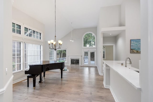 living area featuring light wood-style flooring, high vaulted ceiling, a healthy amount of sunlight, and a glass covered fireplace