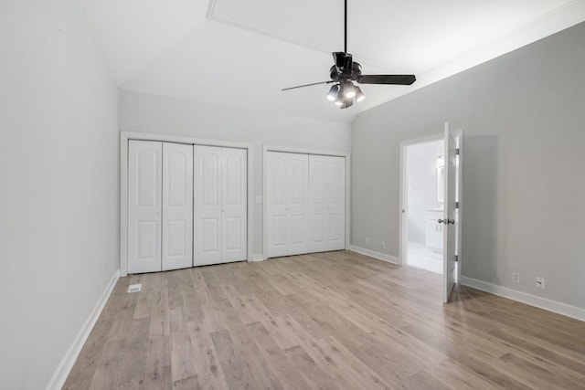 unfurnished bedroom featuring baseboards, multiple closets, vaulted ceiling, and light wood finished floors