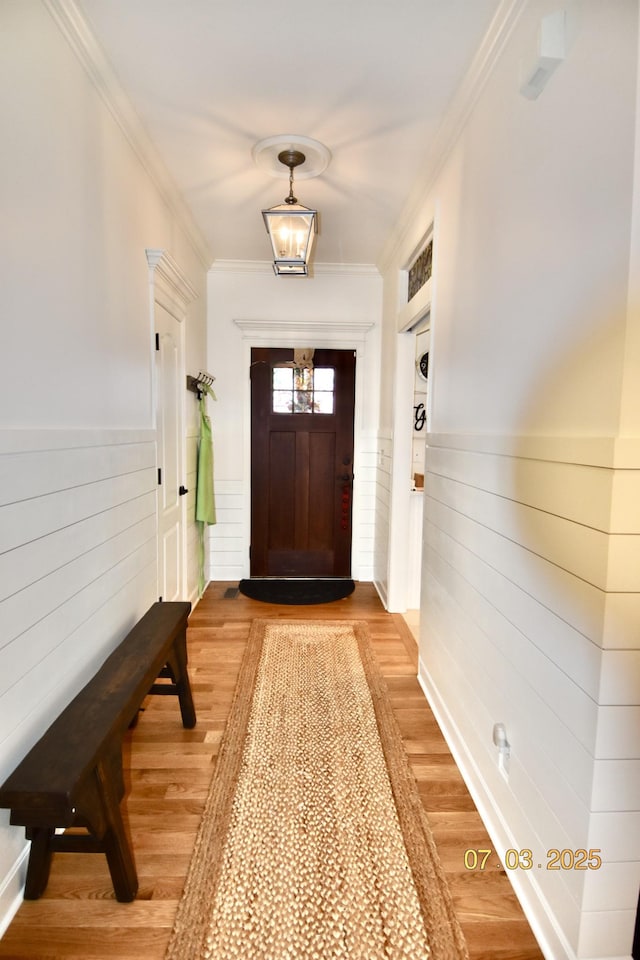 entryway with ornamental molding, light wood finished floors, and wainscoting