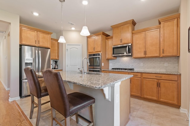 kitchen with an island with sink, light stone countertops, tasteful backsplash, and stainless steel appliances