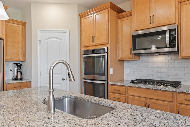 kitchen featuring a sink, decorative backsplash, light stone counters, and appliances with stainless steel finishes