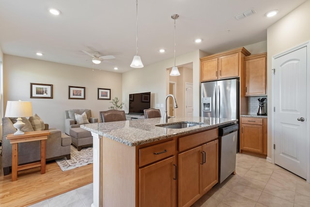 kitchen featuring light stone countertops, open floor plan, a center island with sink, stainless steel appliances, and a sink